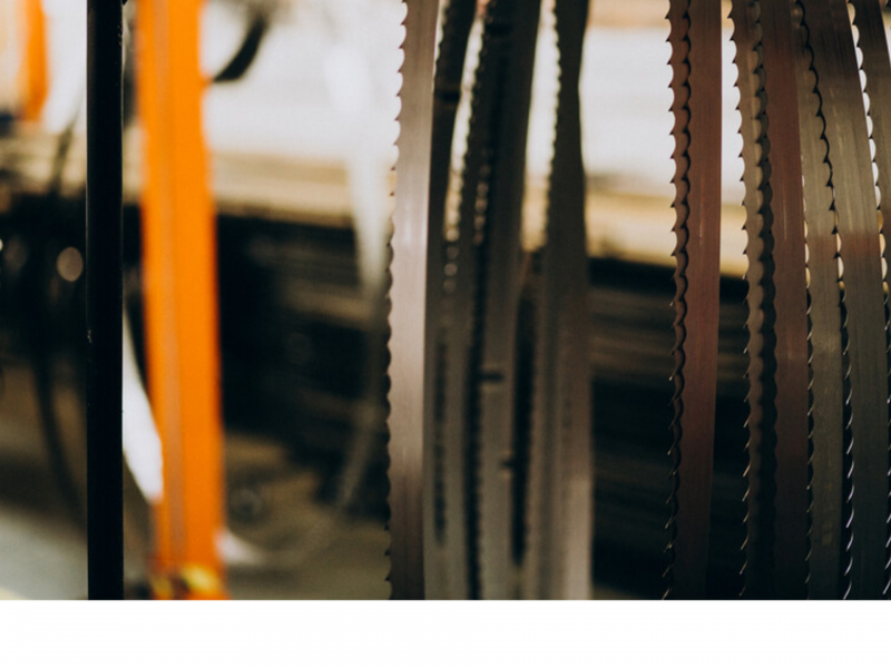 Close-up of hanging industrial band saw blades in a workshop setting, with a blurred background of machinery and workbenches.