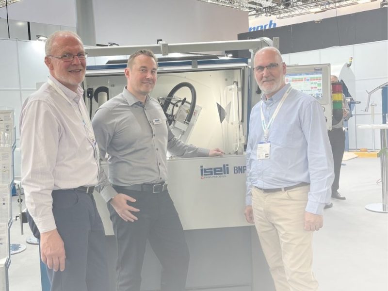 Two members of the team standing in front of the Iseli BNP machine on the Ligna show floor, smiling after a successful supplier meeting.