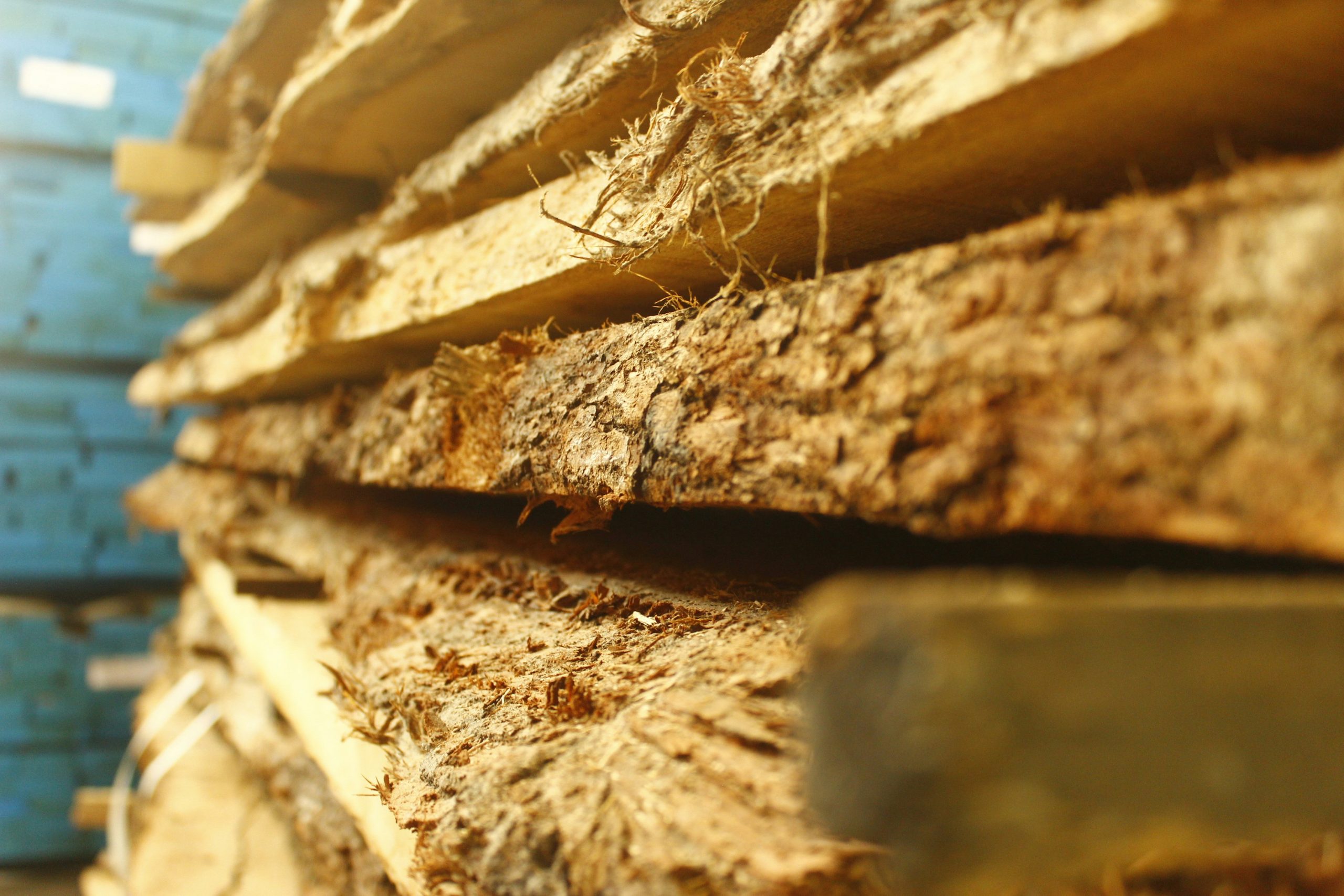 Close‑up view of rough‑cut lumber stacked in a pile, with bark and fibrous edges still attached; the textures and golden tones highlight how little wood is wasted by thin‑kerf sawing.